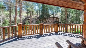 Une terrasse en bois dotée d’une balustrade, qui offre une vue sur une zone boisée et un affleurement rocheux.
