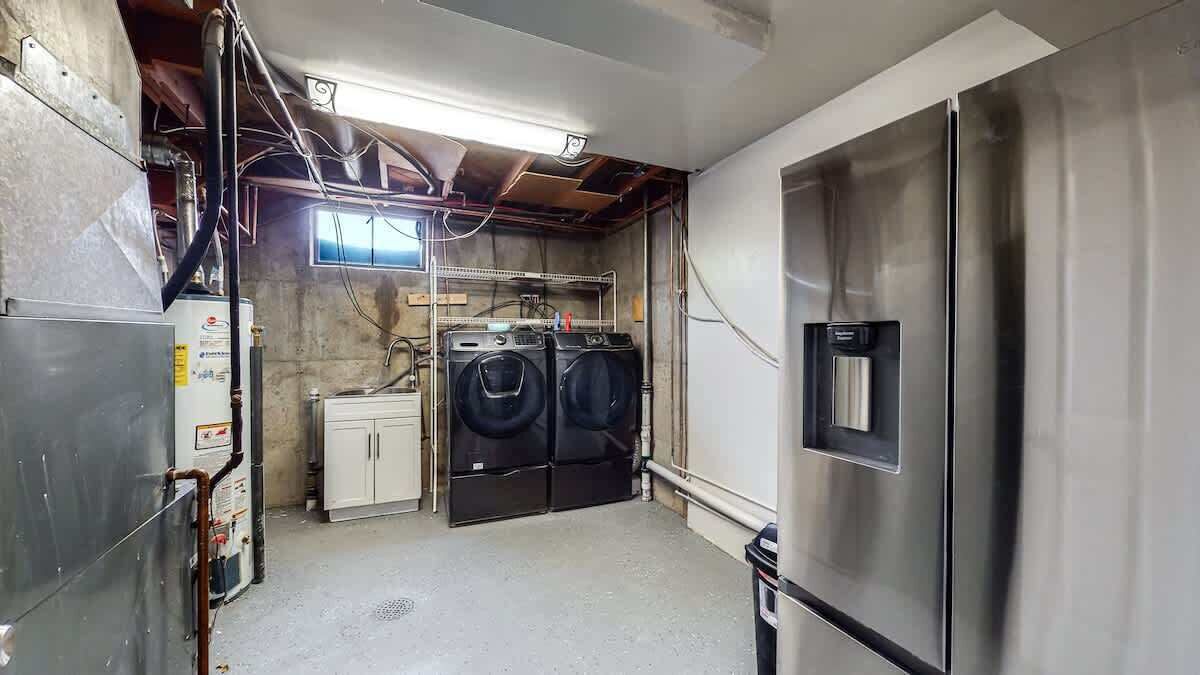 A laundry room with a stainless steel refrigerator, two washing machines, and a water heater.