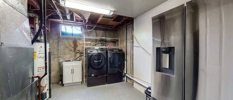A laundry room with a stainless steel refrigerator, two washing machines, and a water heater.