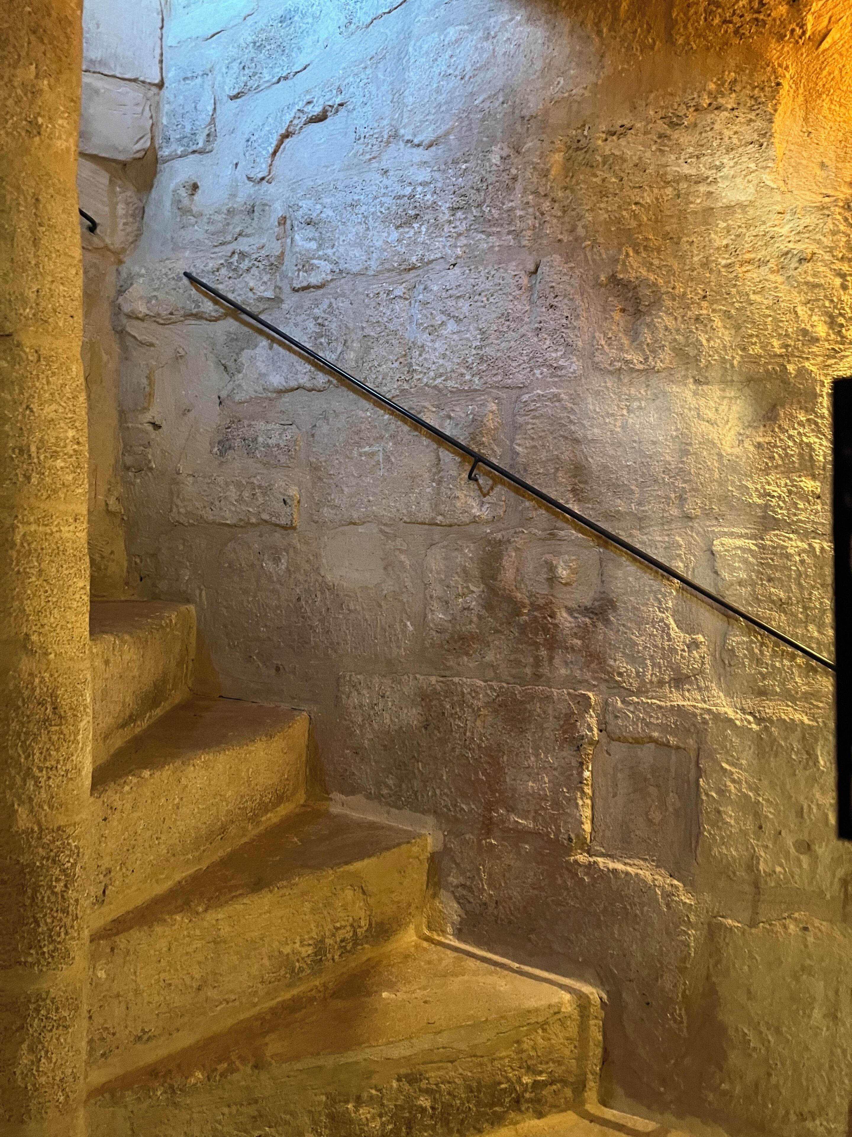 Una escalera de piedra con barandilla de metal que sube a un nivel superior.