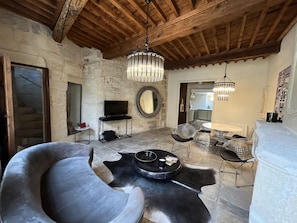 A rustic interior with stone walls, a wooden ceiling, a round mirror, a flat-screen TV, and modern furniture including a sofa and chairs.