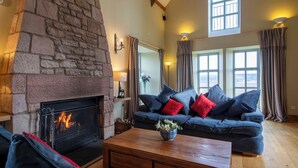 Ein gemütliches Wohnzimmer mit Kamin aus Stein, einem blauen Sofa mit roten Kissen und einem Couchtisch aus Holz.