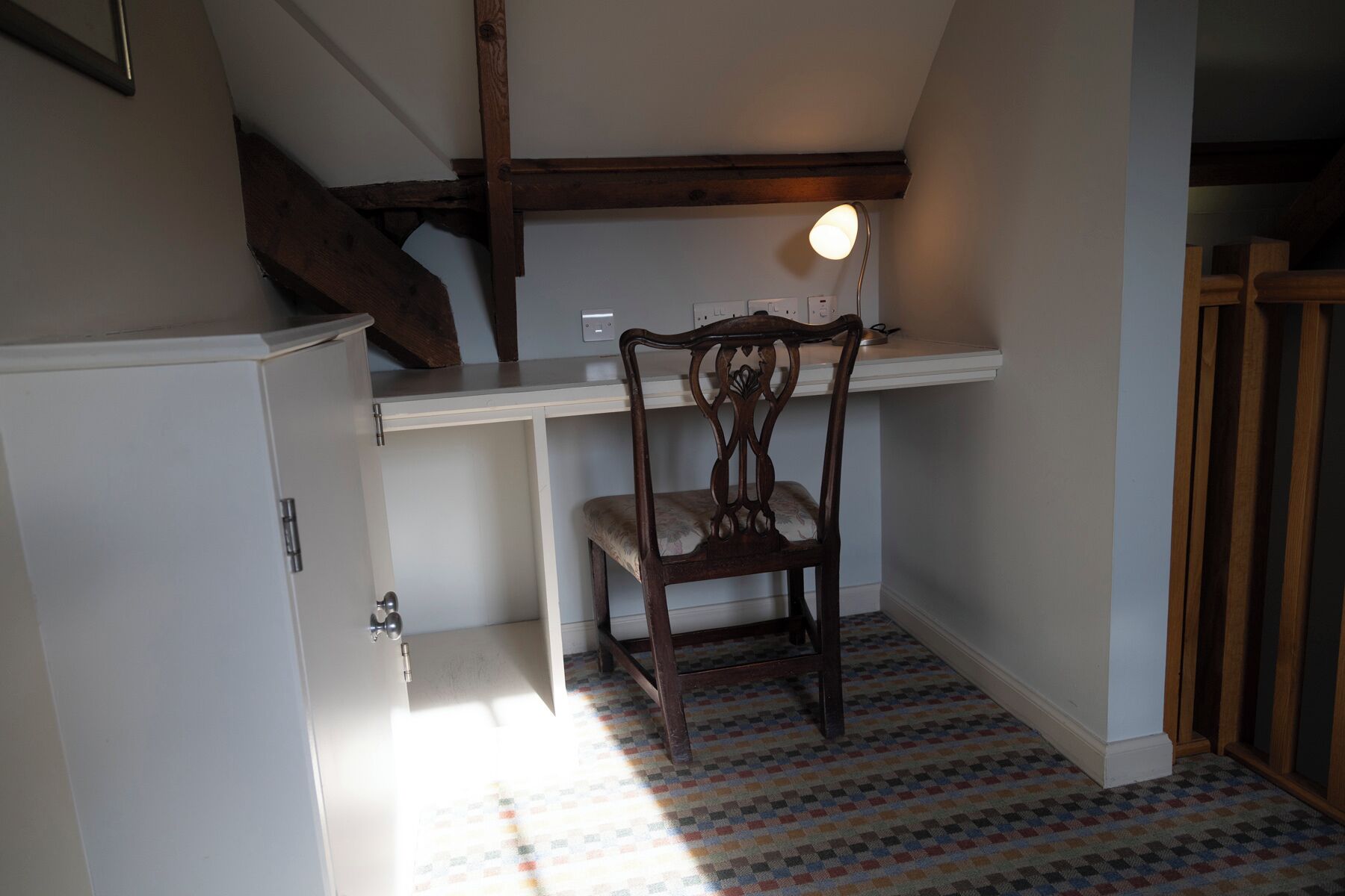 Une petite pièce étroite, avec une chaise en bois, un bureau blanc et un sol à motifs.