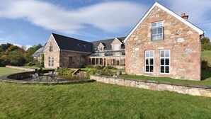 Ein großes Steinhaus mit geneigtem Dach, zahlreichen Fenstern und einem gepflegten Rasen.