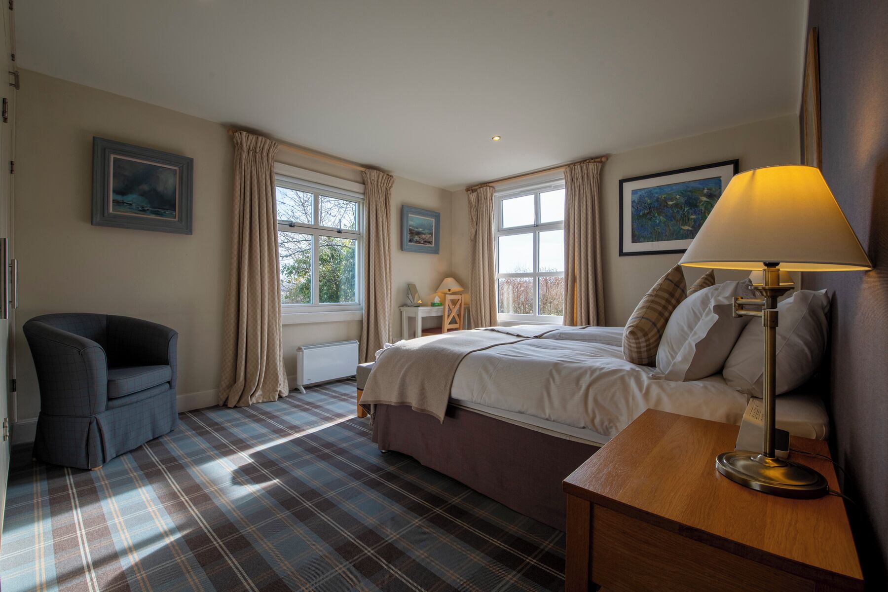 A bedroom with a bed, a chair, a bedside table with a lamp, and a window with curtains.