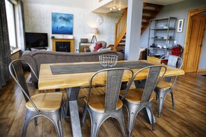 A dining area with a wooden table and metal chairs, a sofa in the background, and a staircase leading to a loft.