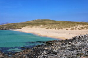 A coastal landscape with a sandy beach, clear turquoise waters, and rocky terrain.
