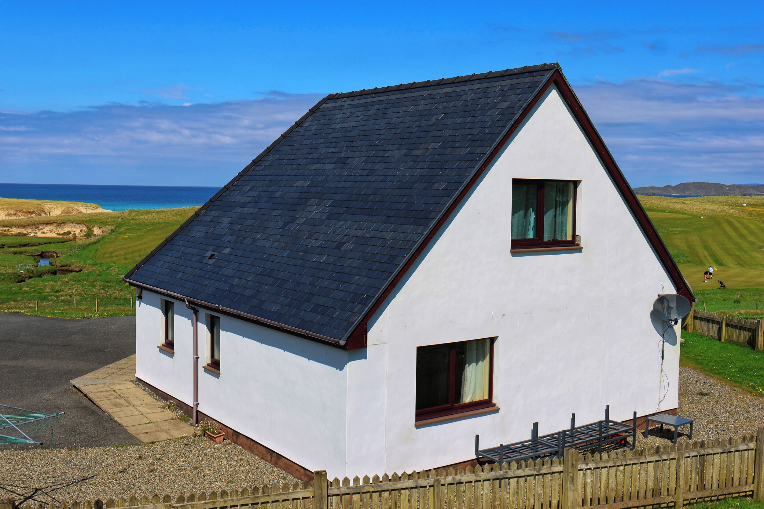 A white house with a dark roof, two windows, and a satellite dish.
