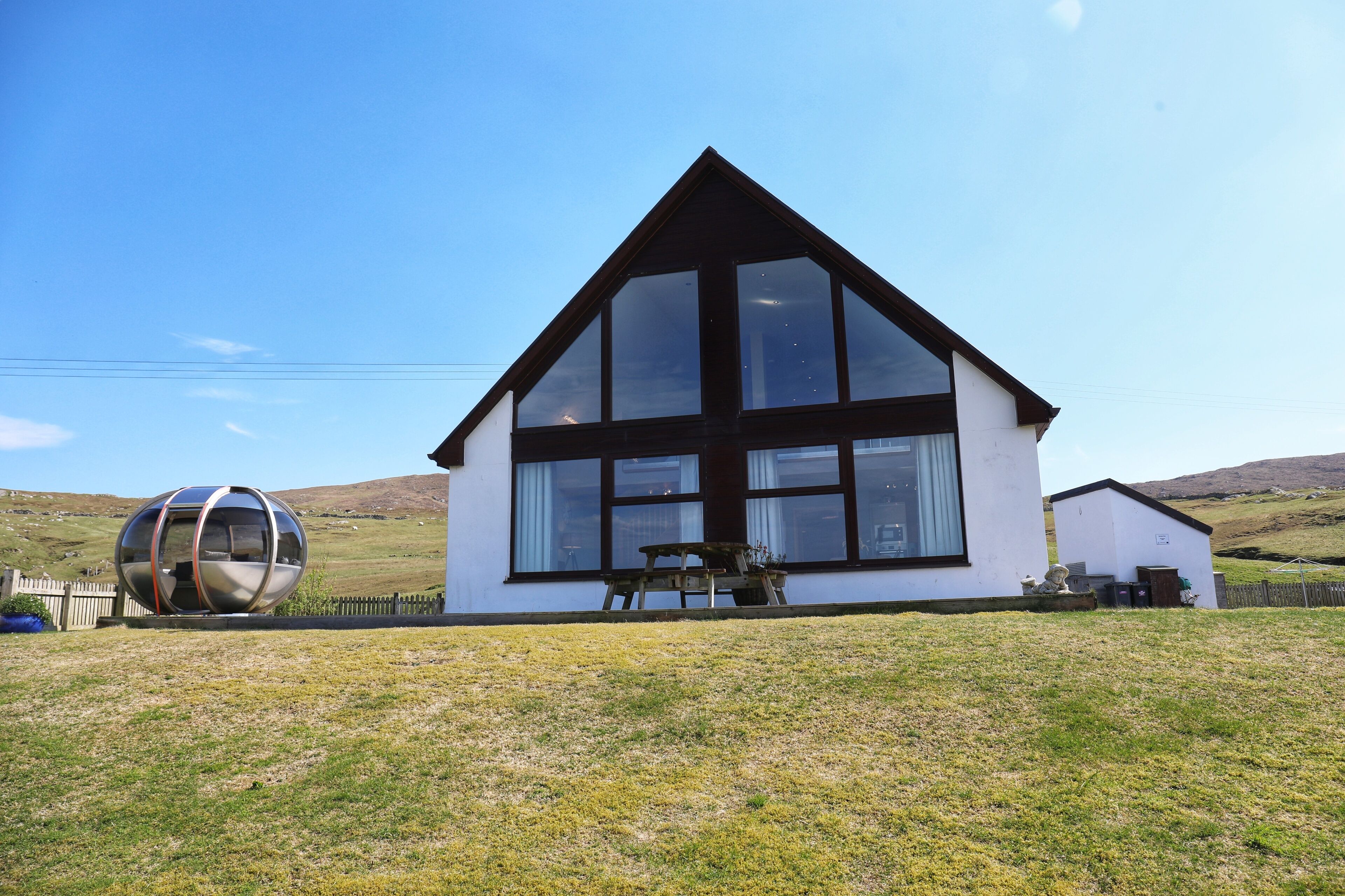 A modern house with a large glass window, a wooden deck, and a spherical sculpture in the yard.