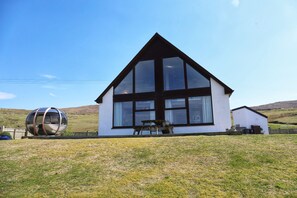 A modern house with a large glass window, a wooden deck, and a spherical sculpture in the yard.