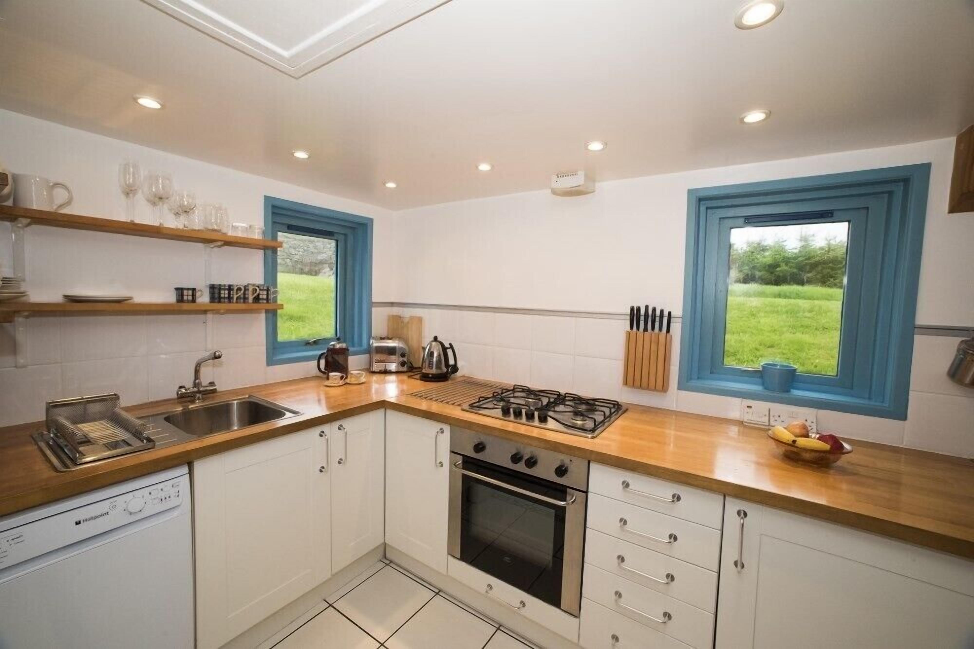 A modern kitchen with white cabinets, a gas stove, a dishwasher, and a large window with a view of greenery.