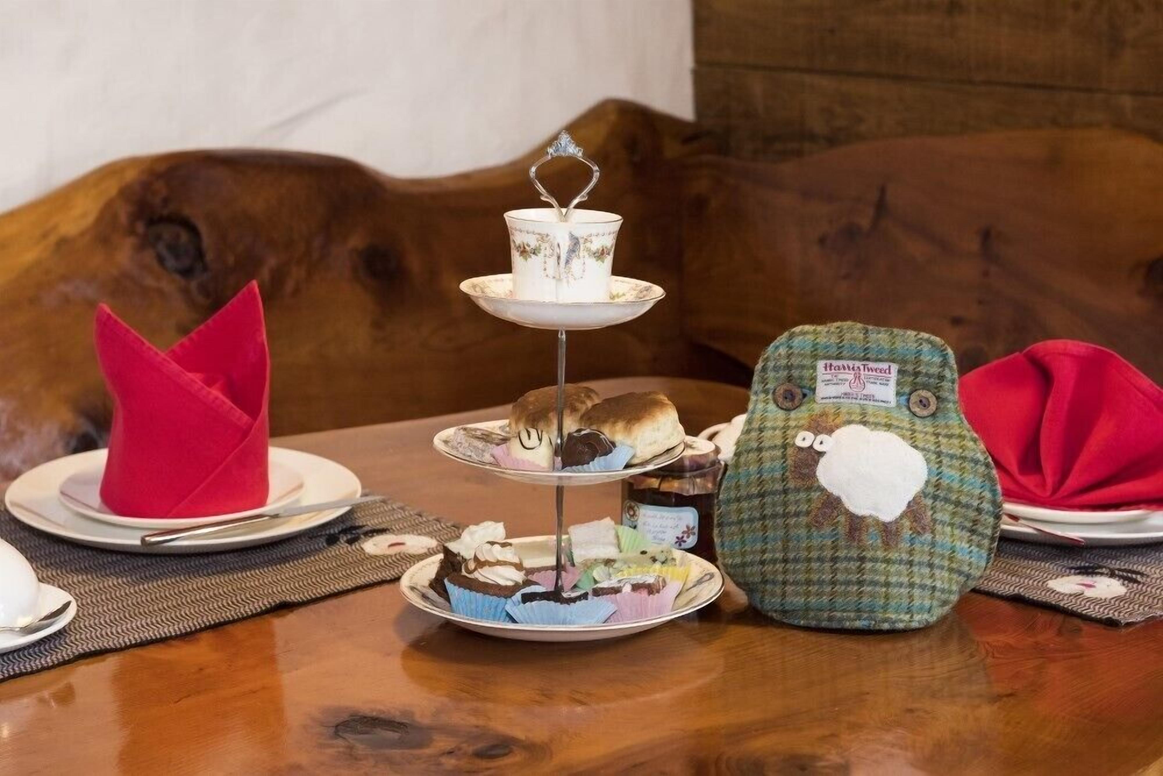 A table with a tiered serving tray holding various pastries, a knitted bag with a sheep design, and a red napkin.