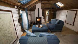 Un acogedor espacio tipo loft con pared de piedra, chimenea, asientos tapizados en azul y tragaluces.