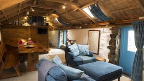 Interior acogedor de una cabaña de madera con una mesa de comedor, asientos tapizados en azul y una pared de piedra.