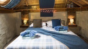 Un dormitorio acogedor en el ático, con techo inclinado, dos camas con ropa de cama azul y luces de cuerda.
