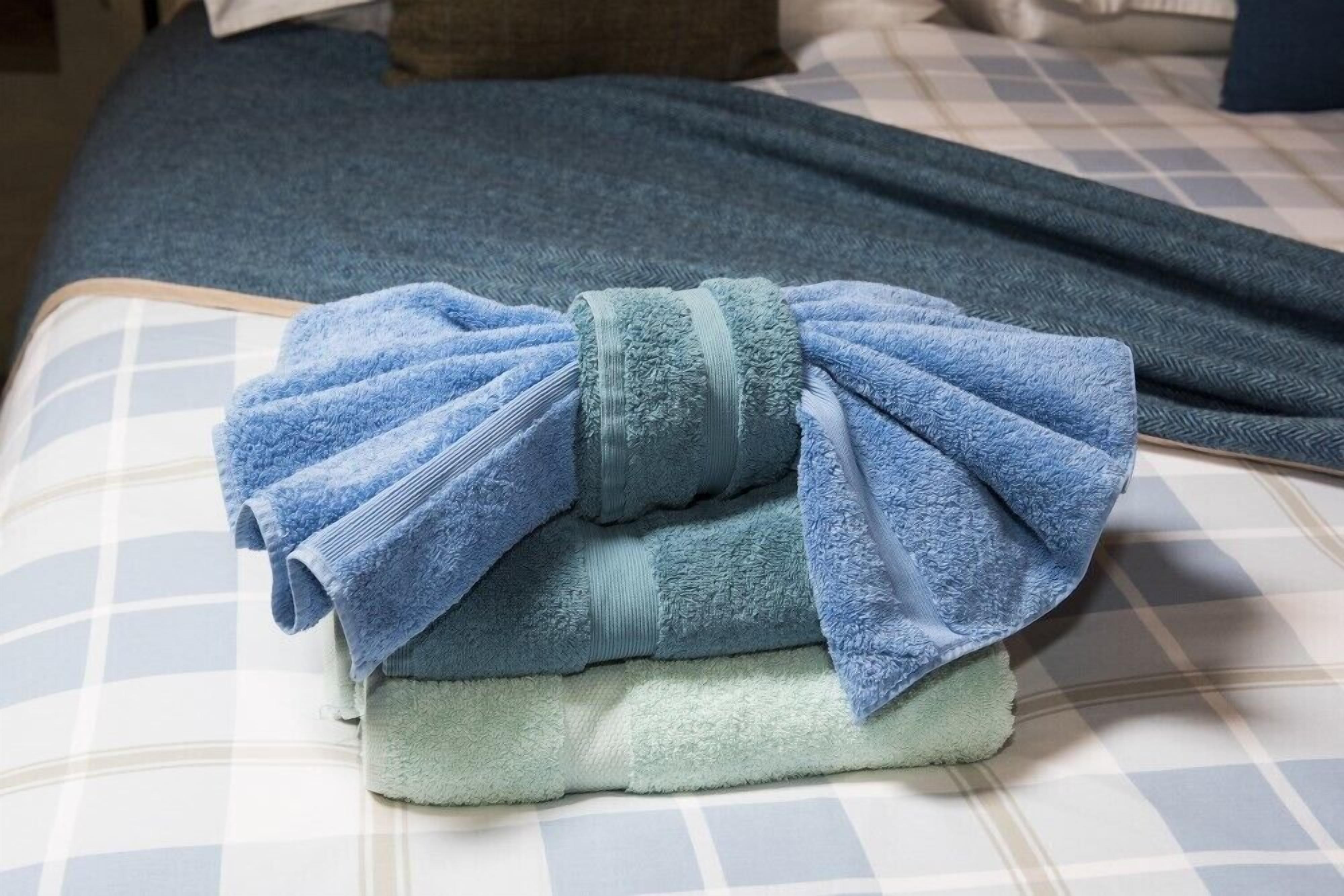 A bed with a blue and white checkered bedspread, a folded blue towel, and a dark blue blanket.