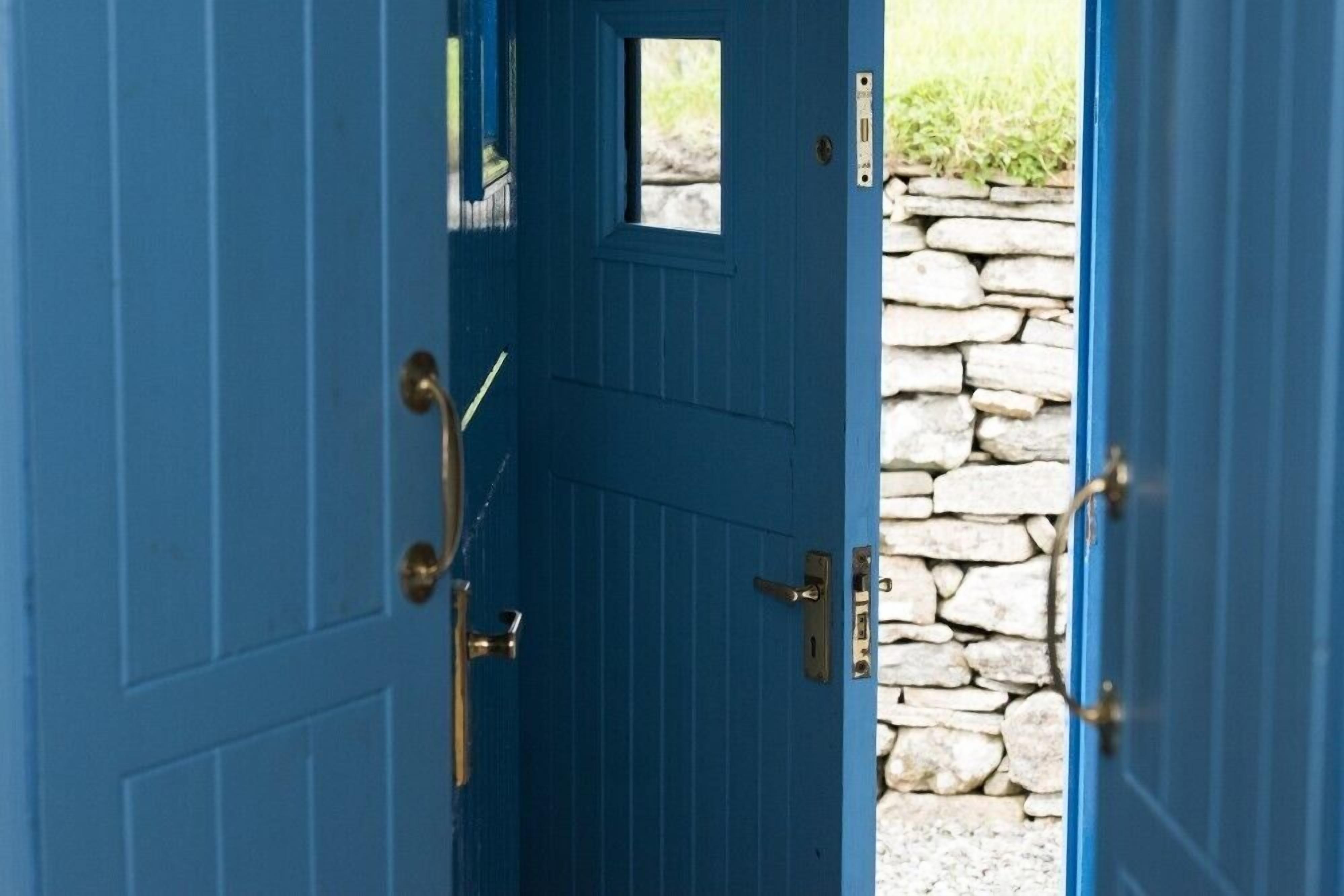 A blue door with a small window and a stone wall visible through the gap.