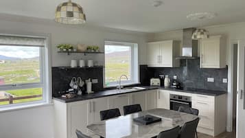 A modern kitchen with white cabinets, a marble countertop, and a dining area with a table and chairs.