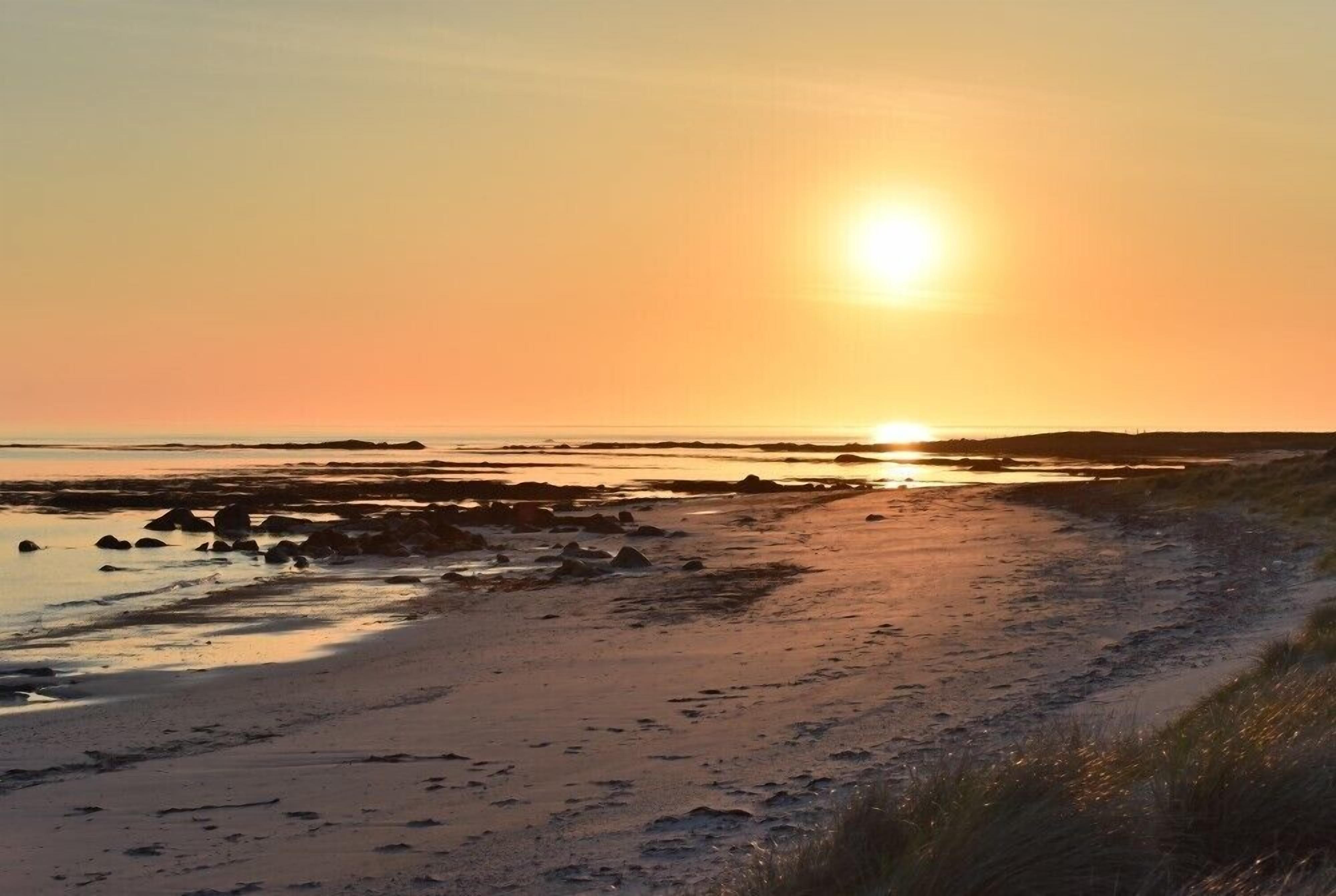 Eine Strandansicht im Sonnenuntergang mit blauem Himmel, ruhigem Wasser und Felsen am Ufer.