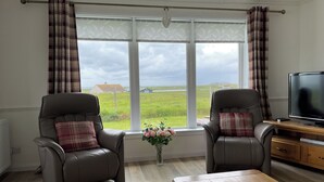 A living room with two leather armchairs, a wooden coffee table, and a television on a wooden stand. - Fuidaigh (South Uist)