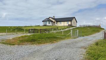 A two-story house with a gravel driveway leading to a wooden gate.