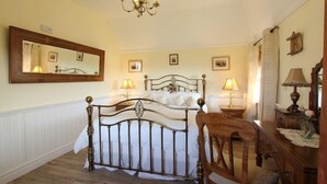 A bedroom with a four-poster bed, a wooden chair, a dresser, and a chandelier. - Smiddy Cottage (South Uist)