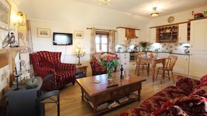 A cozy living room with a wooden coffee table, red patterned sofa, and a television. - Smiddy Cottage (South Uist)