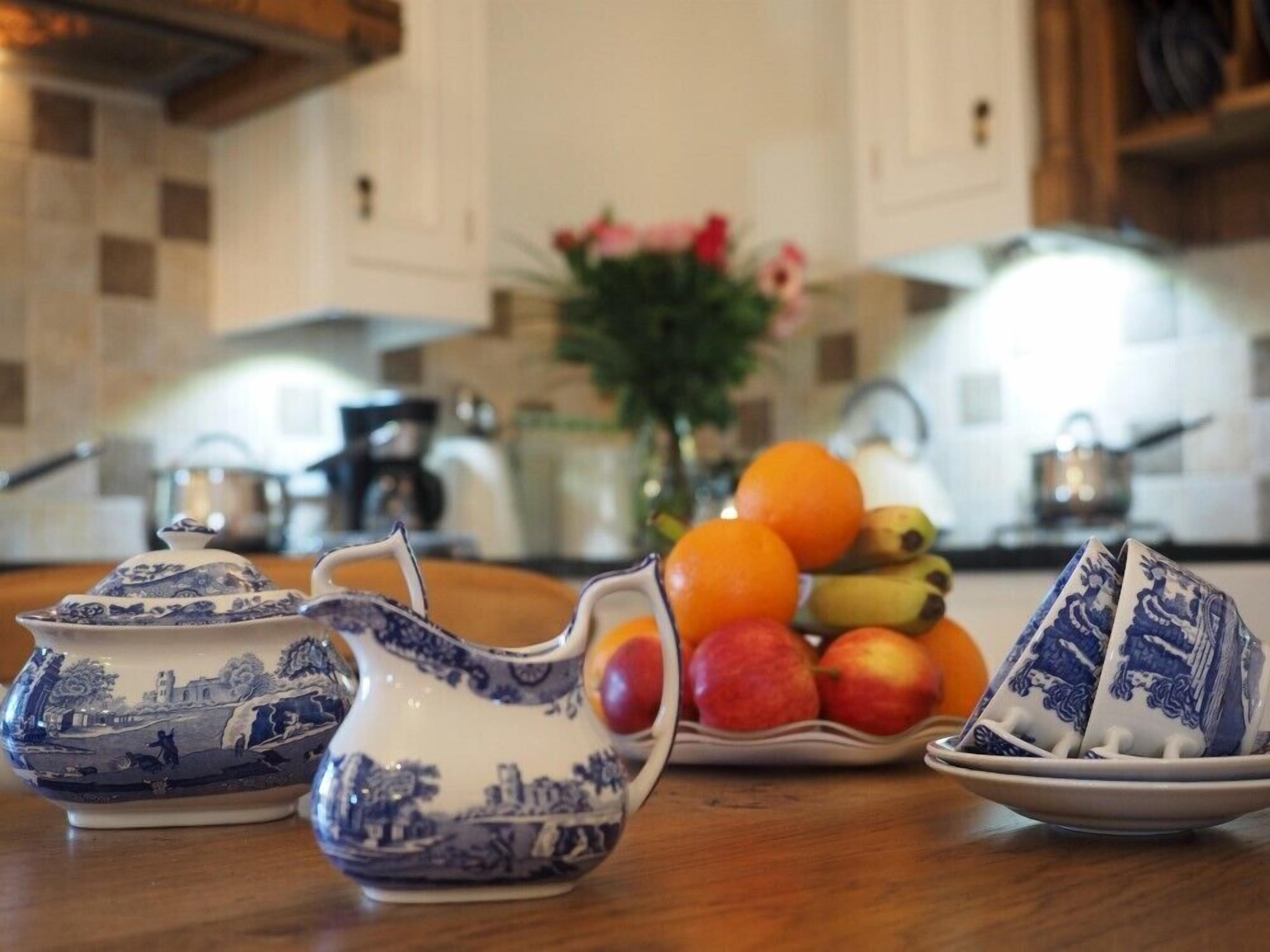 A kitchen with a fruit bowl containing oranges, apples, and bananas, and two blue and white patterned pitchers on the counter.