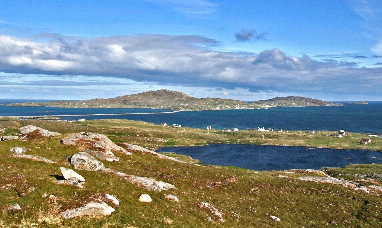 A coastal landscape with rocky terrain, a small body of water, and distant islands.