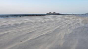 Ein Strand mit glatter, welliger Sandfläche und einer entfernten Hügelkette.