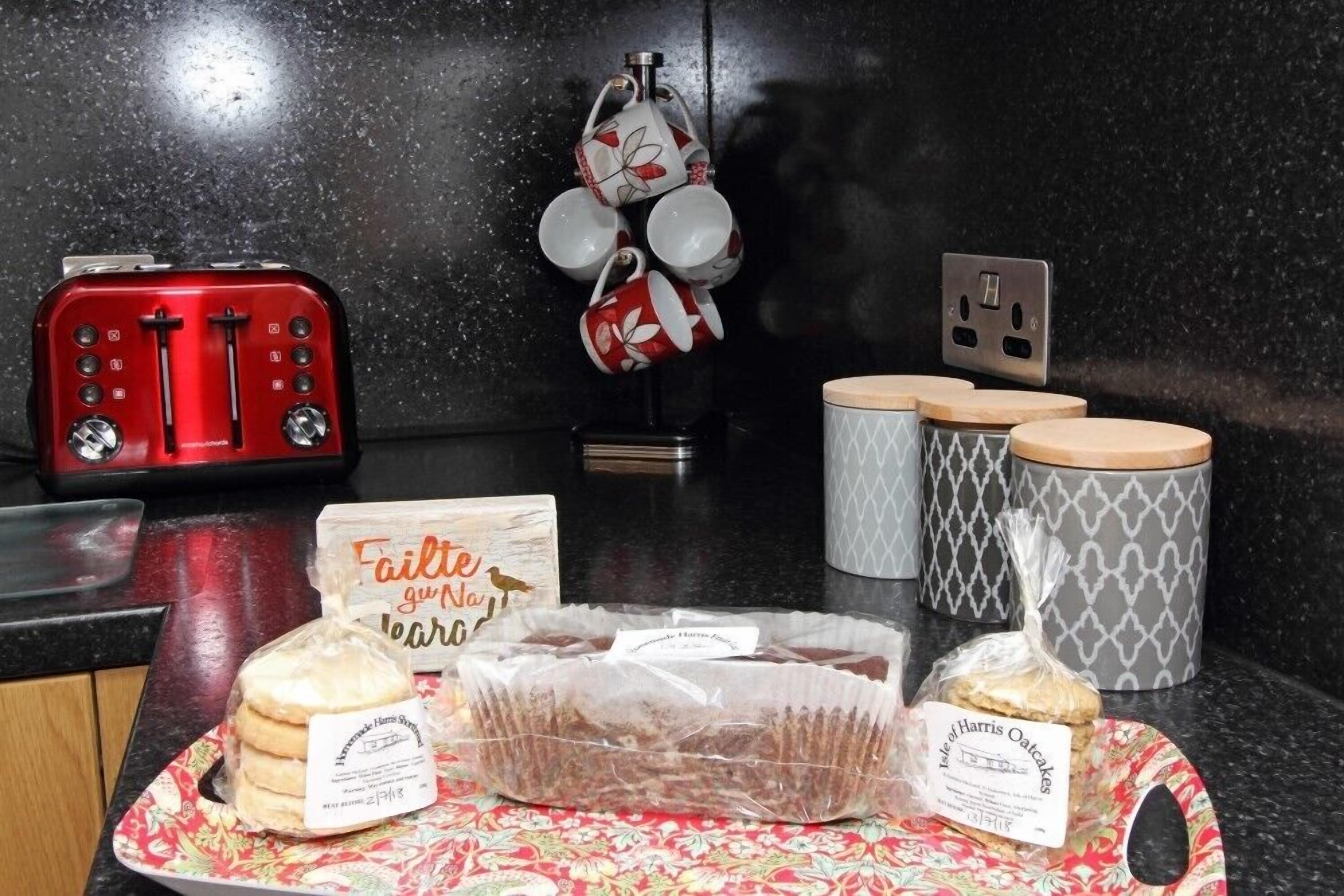 A kitchen counter with a red toaster, a sign that reads "Faitle guppah," and packaged food items including biscuits and oatcakes.