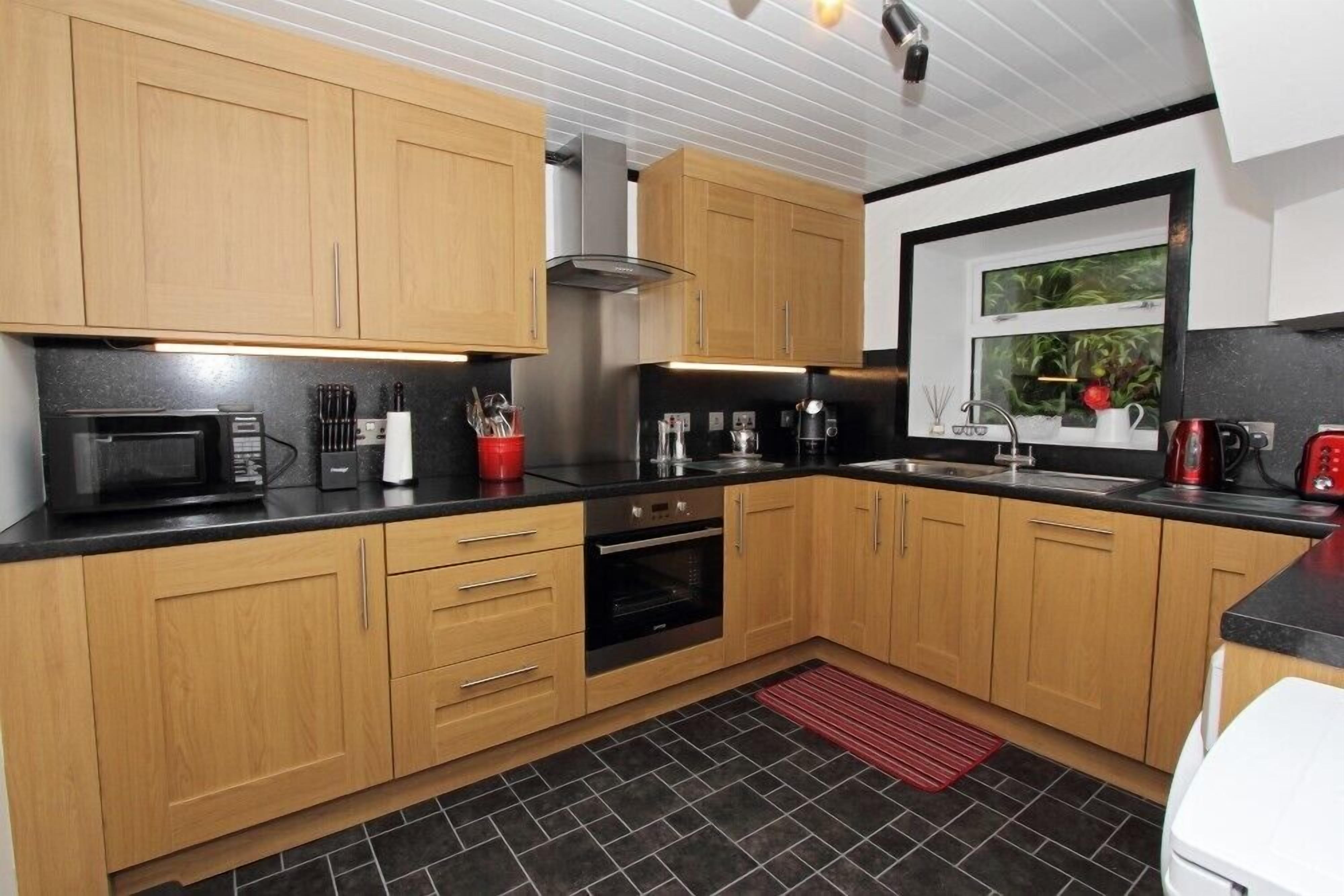 A modern kitchen with wooden cabinets, a black countertop, a microwave, an oven, and a window with a view of greenery.