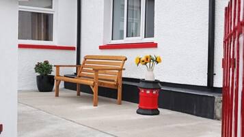 A wooden bench outside a building with white walls and red accents.