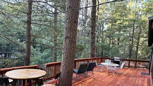 Eine Holzterrasse mit rundem Tisch und Stühlen, umgeben von Bäumen.