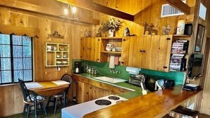 Ein Holzinnenraum mit Küchenbereich, darunter ein Esstisch, Stühle und ein Barbereich.