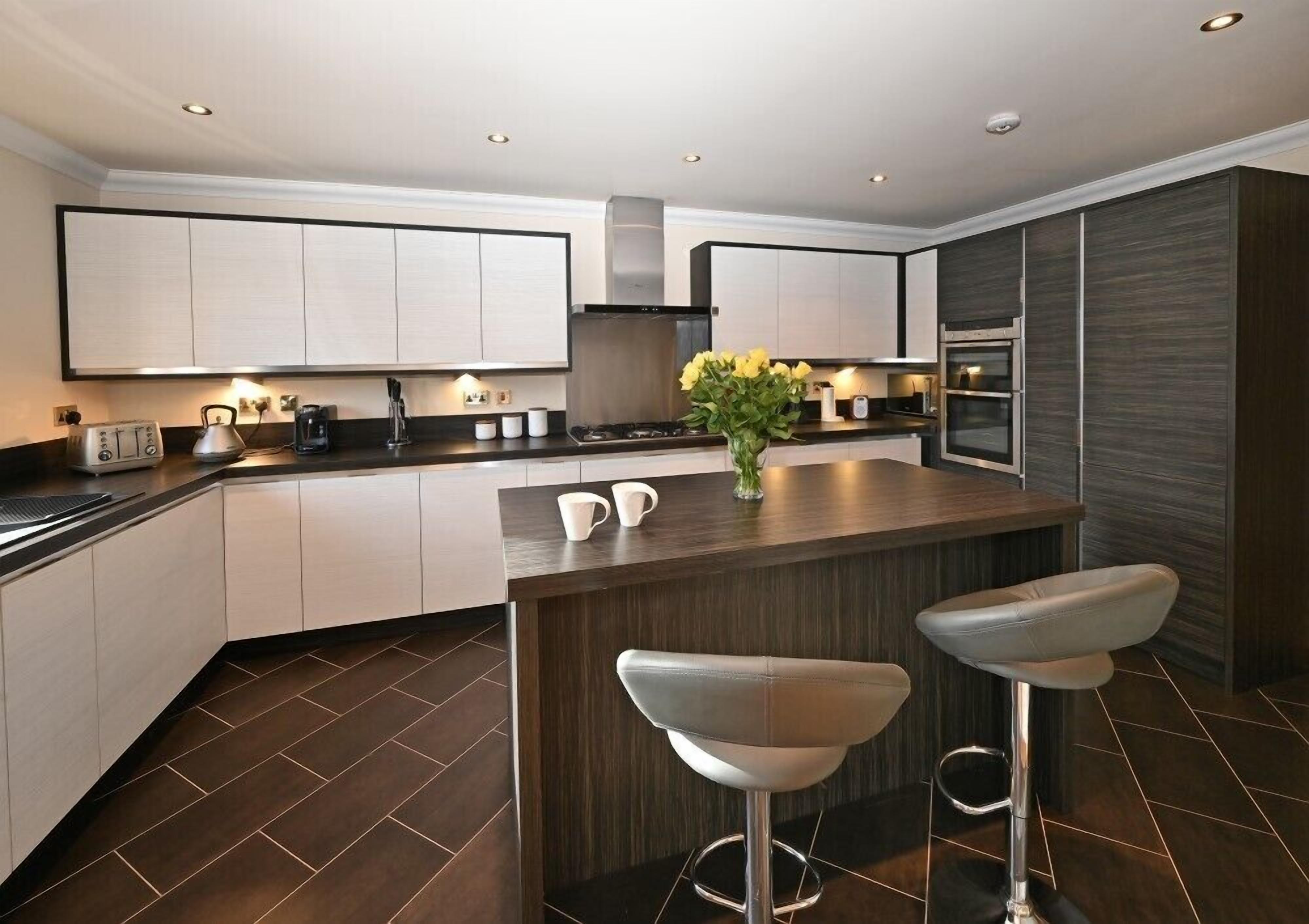 Een moderne keuken met donker houten vloeren, witte kasten, een centraal eiland met barkrukken en een inbouwoven.