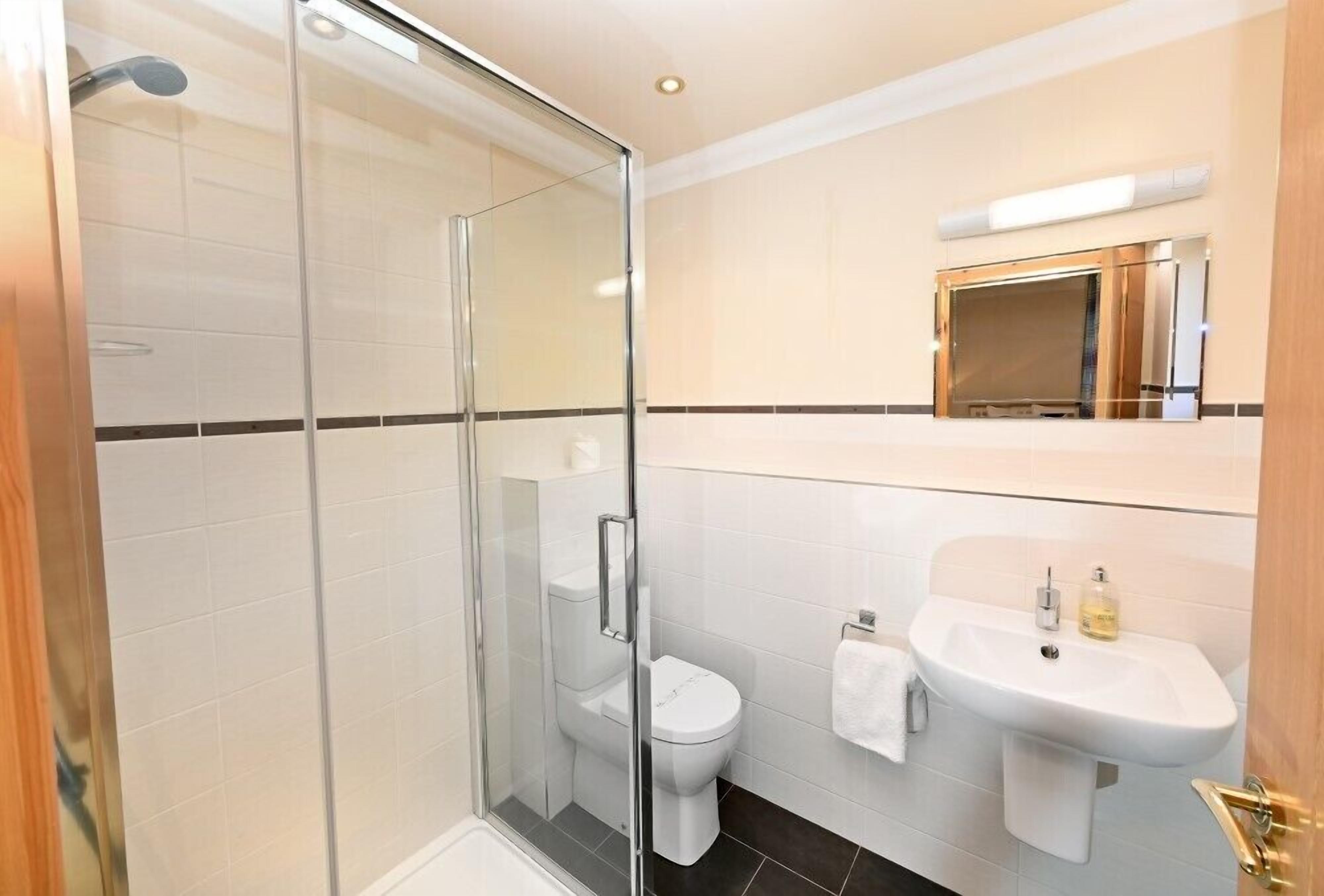 A modern bathroom with a glass-enclosed shower, a white toilet, and a sink with a mirror above it.