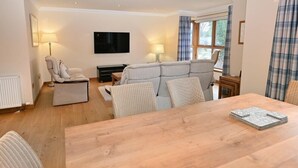 Un salon spacieux avec une table à manger en bois, un canapé gris et un téléviseur à écran plat fixé au mur.