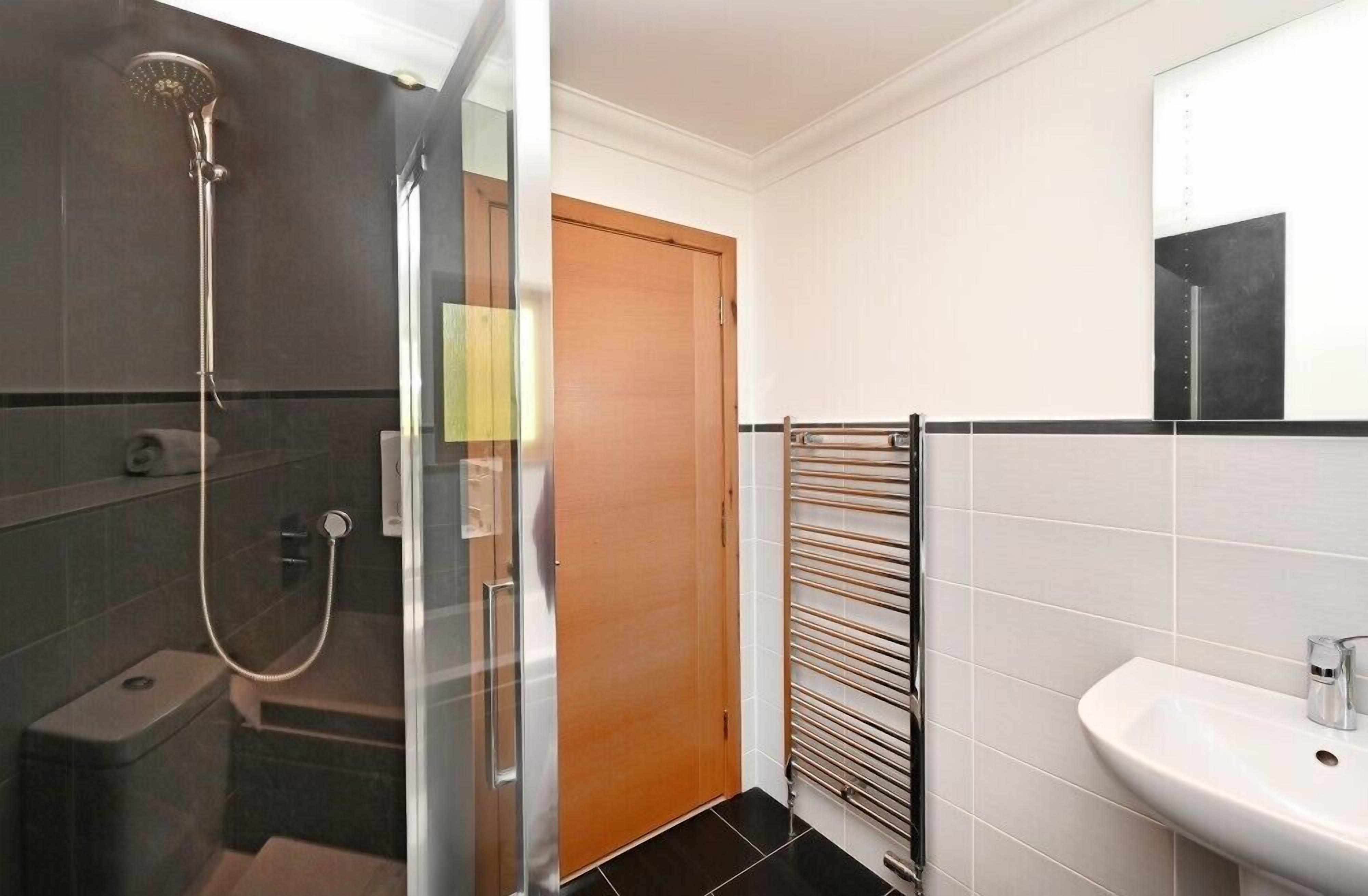 Une salle de bain moderne avec une douche à parois de verre, une porte en bois, un porte-serviettes et un lavabo blanc.