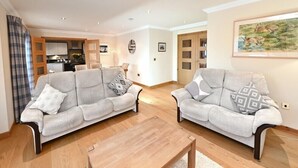 Un salon avec deux canapés gris, une table basse en bois et, au fond, une cuisine.