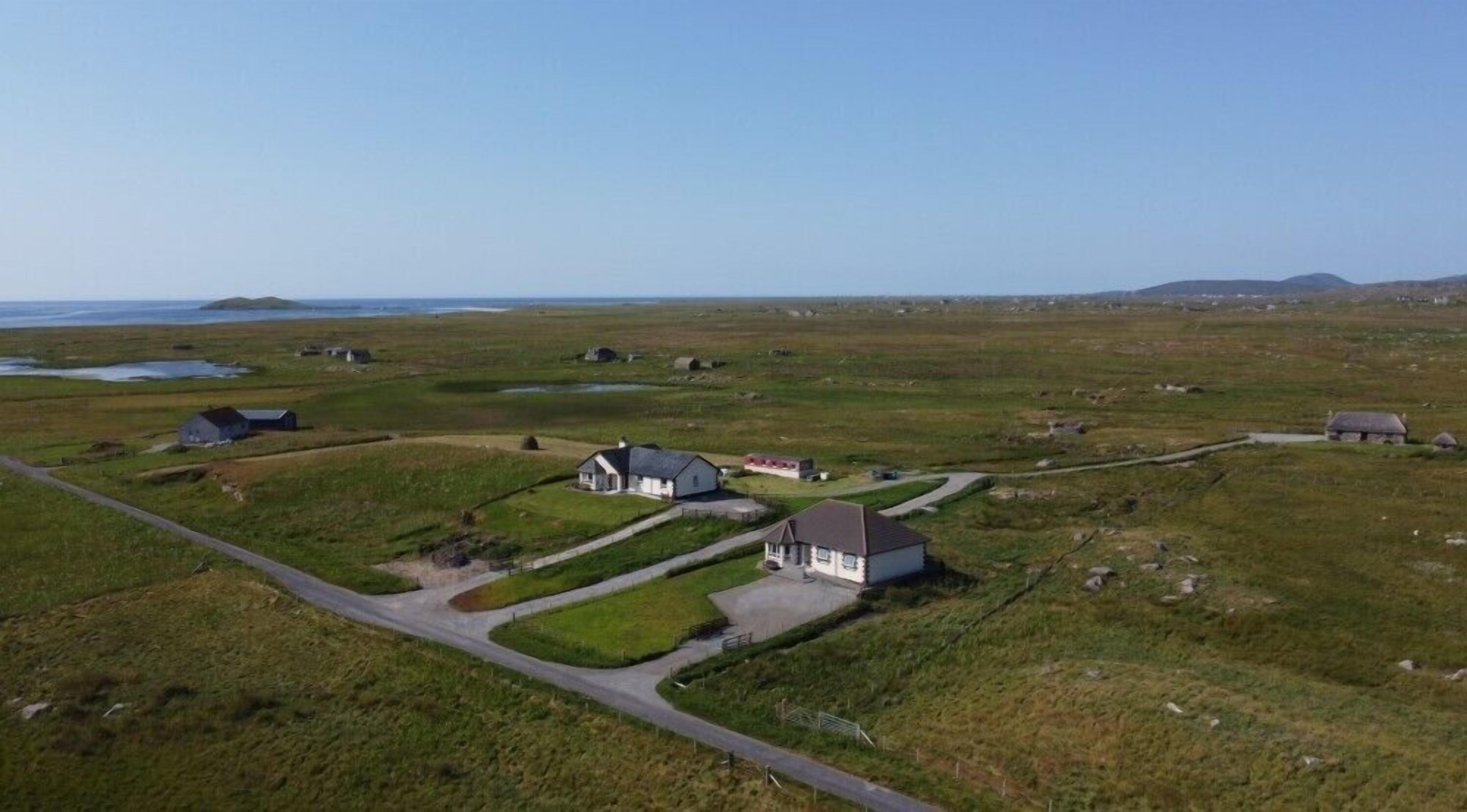 Un paysage rural parsemé de maisons, avec une route sinueuse et une étendue d’eau visible au loin.