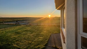 A view from a window overlooking a grassy field with a fence and a gate, during sunset. - Lingeigh (South Uist)
