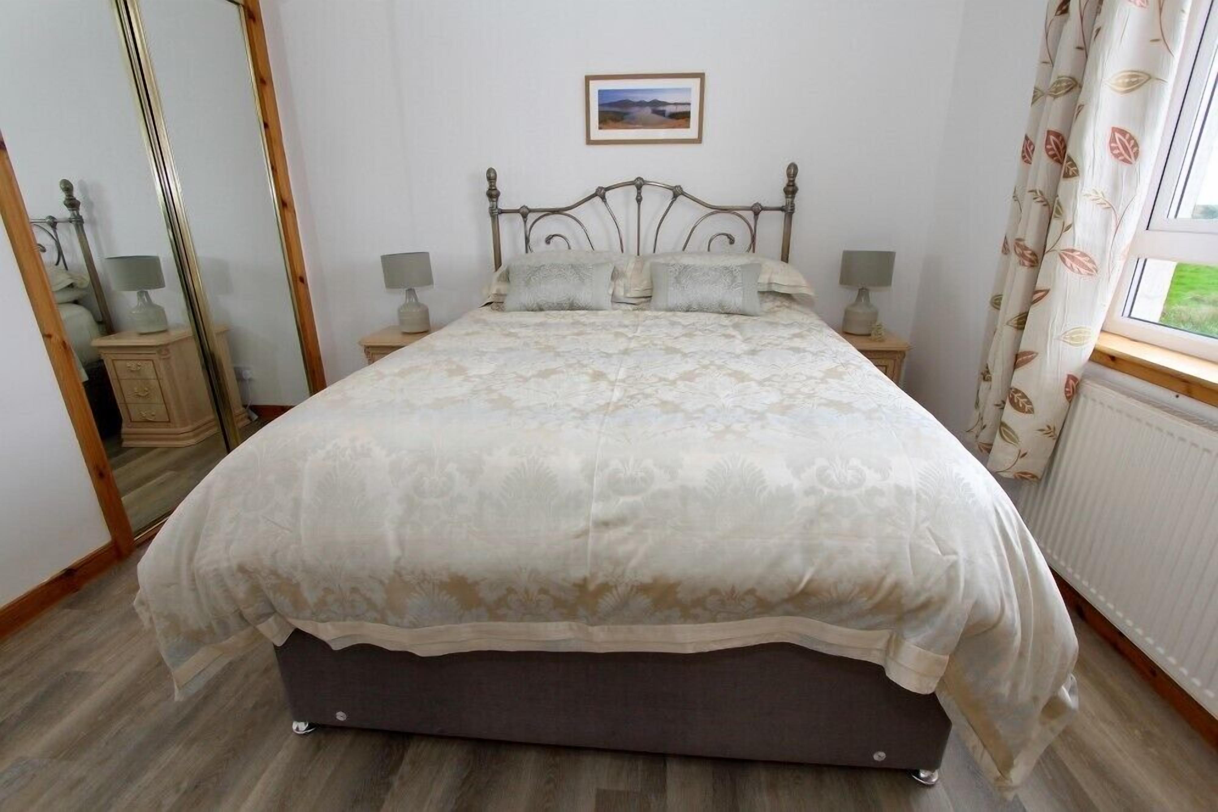 Une chambre à coucher avec un lit, des tables de chevet, un miroir et une fenêtre avec des rideaux.
