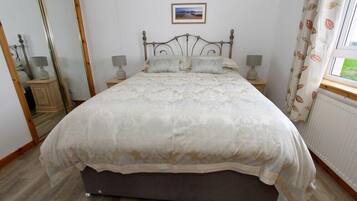 Une chambre à coucher avec un lit, des tables de chevet, un miroir et une fenêtre avec des rideaux.