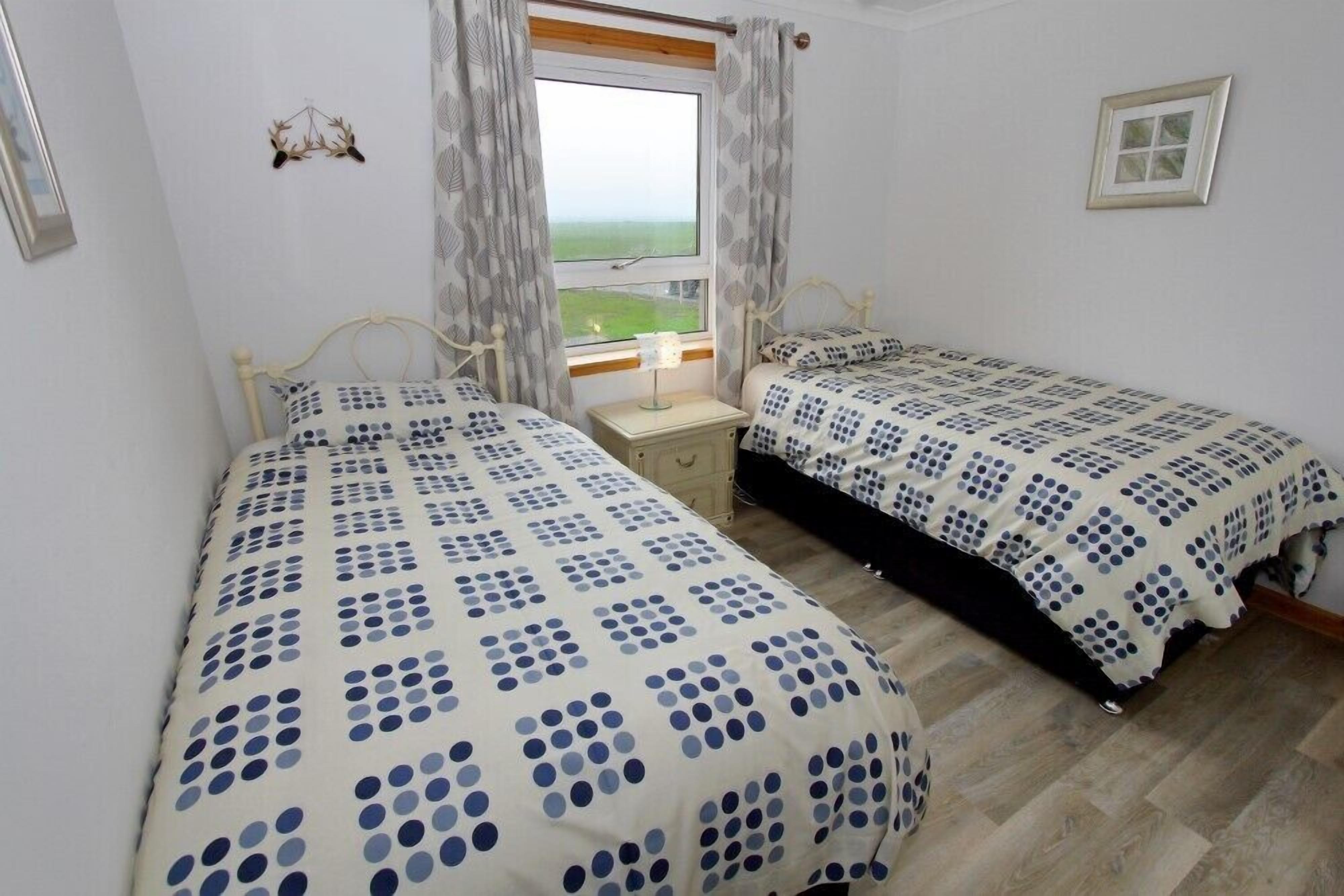 Een slaapkamer met twee bedden, een raam met uitzicht en een klein nachtkastje.
