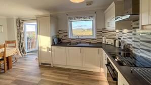 A modern kitchen with a large window, wooden flooring, and a dining area with a table and chairs. - Lingeigh (South Uist)