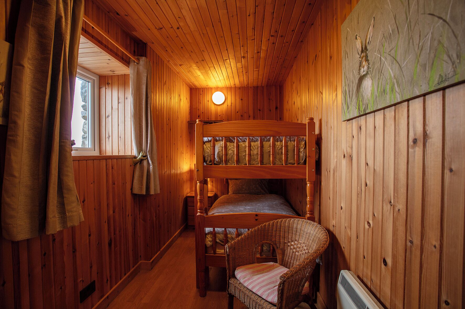 A wooden cabin interior with a bunk bed, a wicker chair, and a radiator.