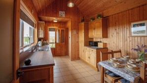 A wooden cabin interior with a kitchen, dining area, and a window with a view. - Kelp Cottage (South Uist)