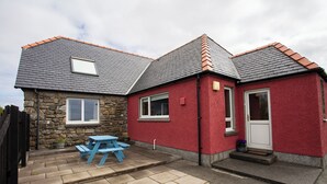 A two-story house with a stone facade and red exterior. - Kelp Cottage (South Uist)