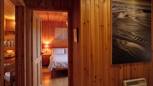 A wooden cabin room with a bed, a nightstand, a lamp, and a framed picture on the wall. - Kelp Cottage (South Uist)